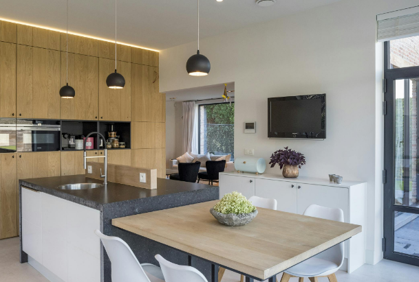 Moderne open keuken met houten kastenwand, zwart kookeiland, ronde eetkamertafel en grote ramen die uitkijken op de tuin.