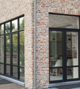Zwarte aluminium ramen en deur in industriële staallook, geplaatst in een klassieke rode bakstenen gevel met grote glaspartijen voor maximale lichtinval.