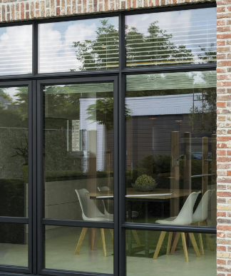 Zwarte aluminium raam- en deurpartij in een bakstenen gevel met zicht op een moderne eetruimte met witte stoelen en houten tafel