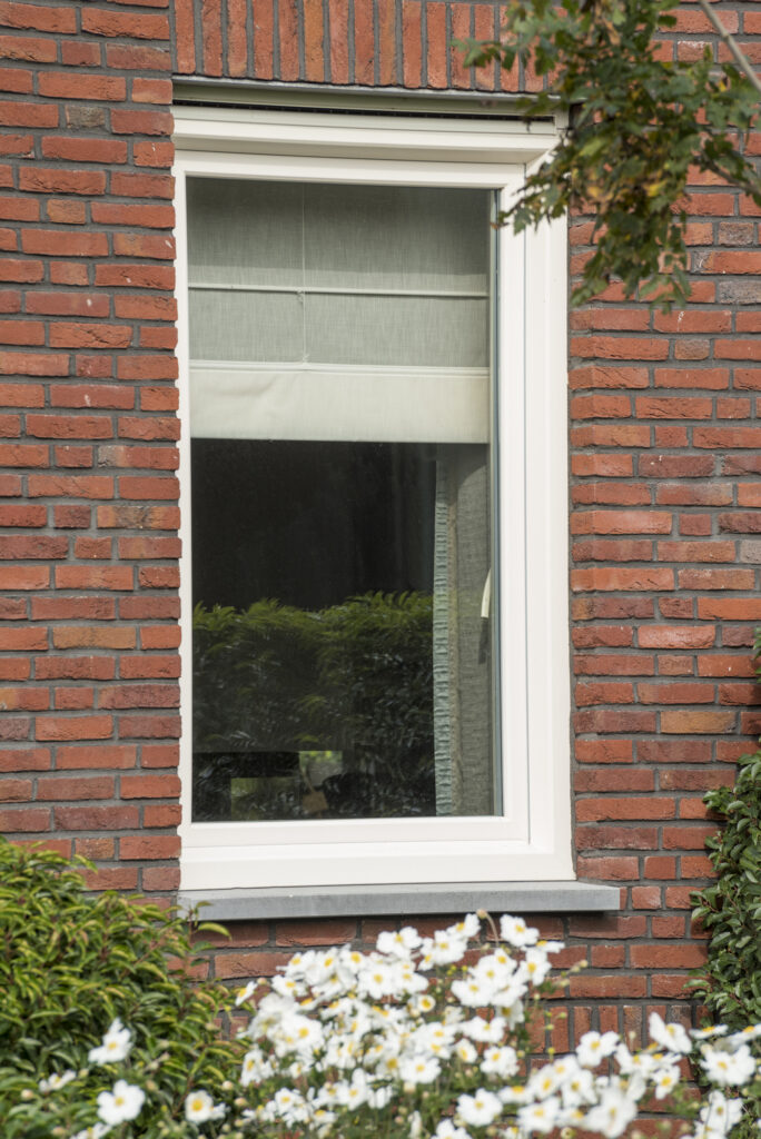 Wit aluminium raam in een klassieke rode bakstenen gevel, geplaatst door Bruvo.