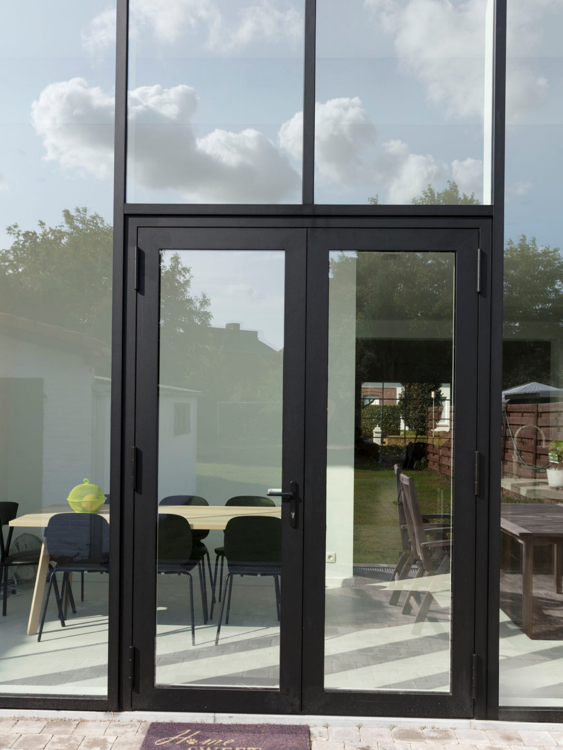 Zwarte aluminium deur met grote glaspartijen van Bruvo, die een moderne en elegante overgang tussen binnen en buiten creëert met veel natuurlijk licht.