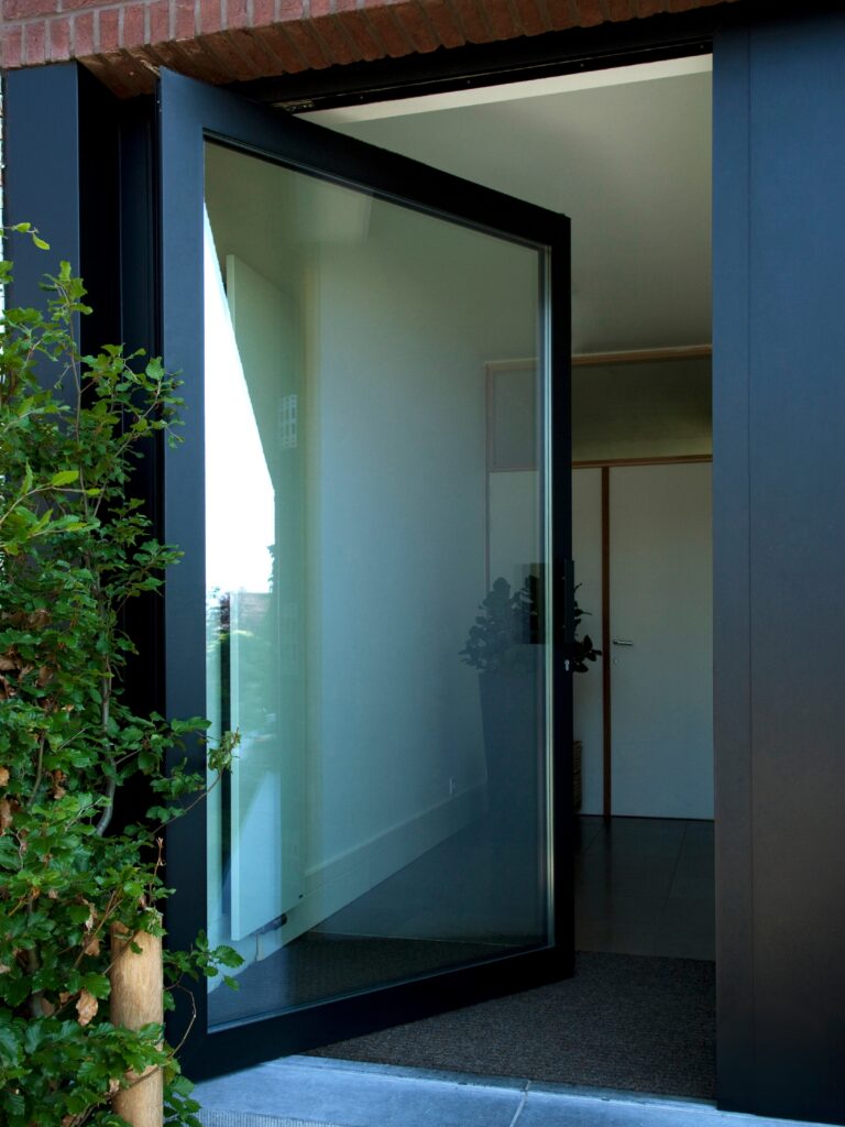 Strakke aluminium pivotdeur van Bruvo met groot glasoppervlak, perfect geïntegreerd in een moderne gevel voor een stijlvolle en lichtrijke entree.