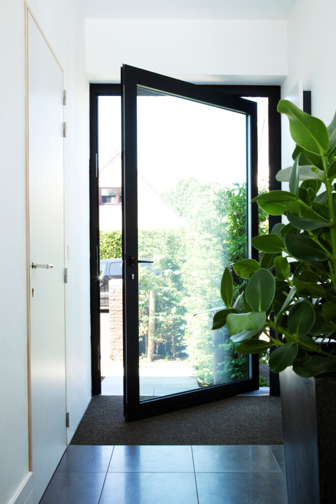 Zwarte aluminium pivotdeur van Bruvo in moderne woning, met groot glasvlak dat zorgt voor maximale lichtinval en een elegante overgang tussen binnen en buiten.