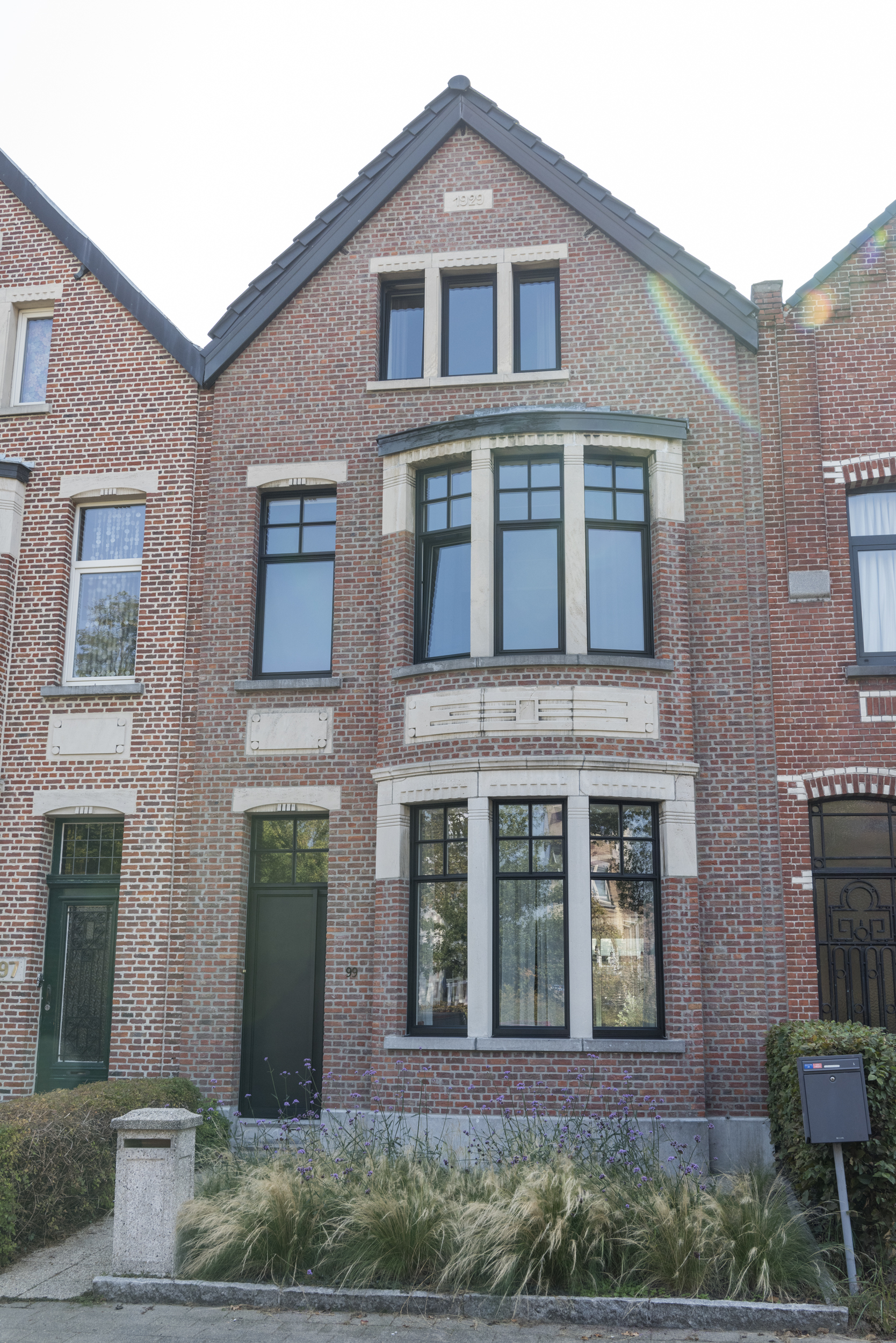 Moderne voorgevel met antracietgrijze raamprofielen en een strakke aluminium voordeur in Schoten.