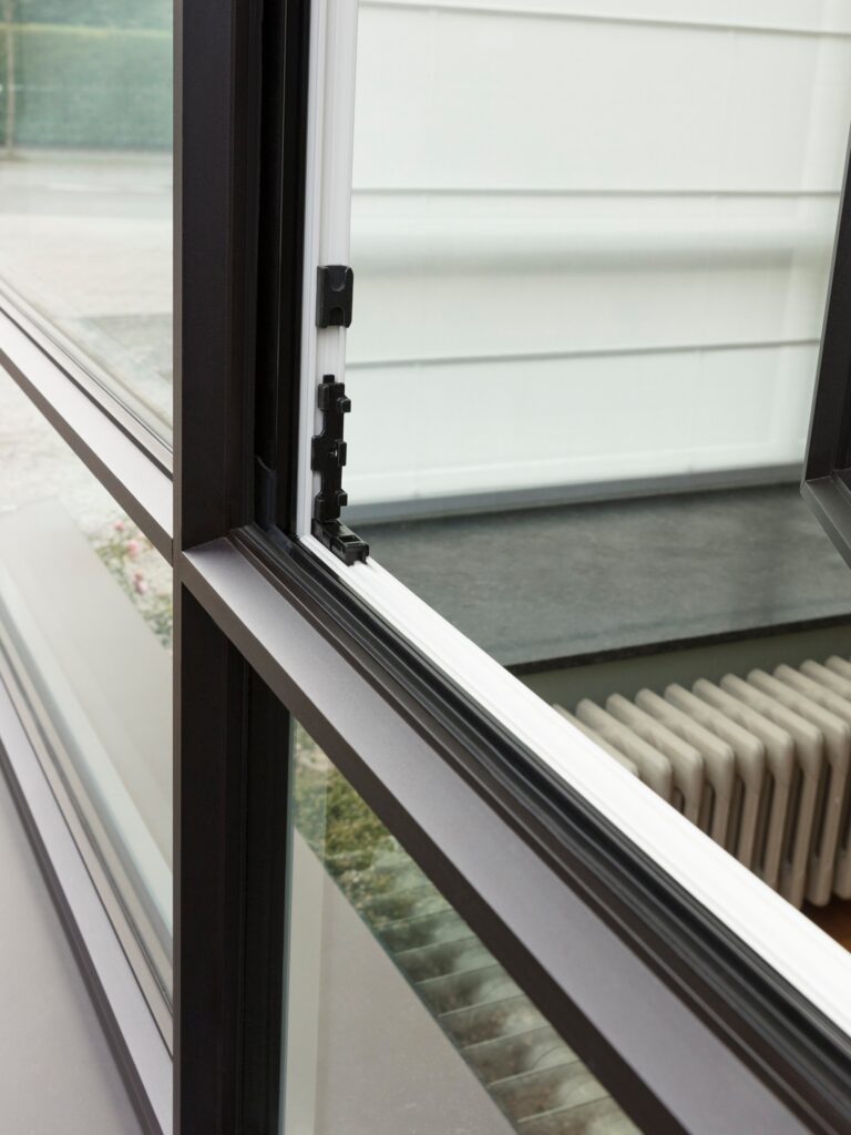 Close-up van een openstaand aluminium raam met moderne zwarte profielen en strak design, geplaatst door Bruvo voor een eigentijdse woning met oog voor detail en kwaliteit.