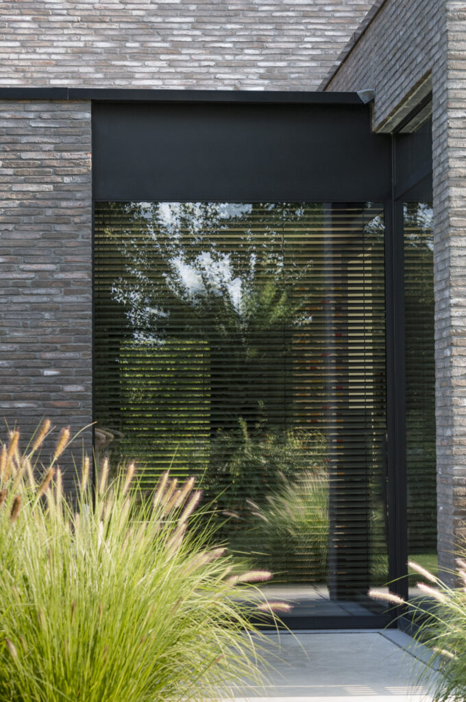 Zwart aluminium raam met geïntegreerde zonwering in moderne gevel, gerealiseerd door Bruvo.