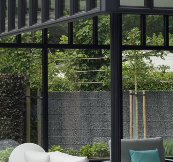 Moderne aluminium veranda met slanke zwarte profielen en grote glaspartijen, uitkijkend op een groene tuin met gabion-afsluiting