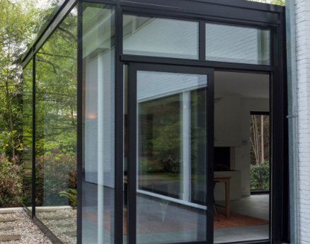 Moderne aluminium schuifdeur met slanke profielen die toegang geeft tot een helder balkon met glazen balustrade en uitzicht op de omgeving.
