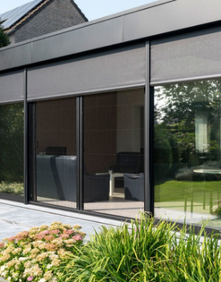 Moderne aanbouw met zwarte aluminium schuiframen en geïntegreerde screens, uitkijkend op een onderhoudsvriendelijke tuin.